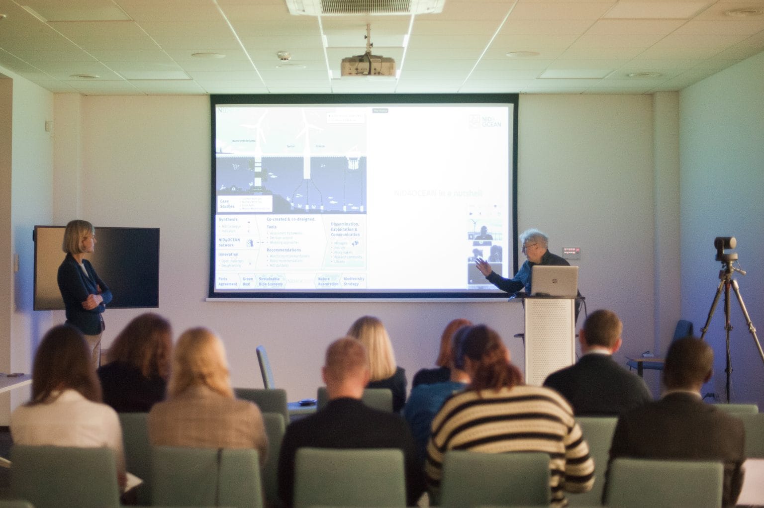 dr. Artūras Razinkovas-Baziukas from KU standing in front of a projection of a PowerPoint, explains the challenge to a room of seated participants